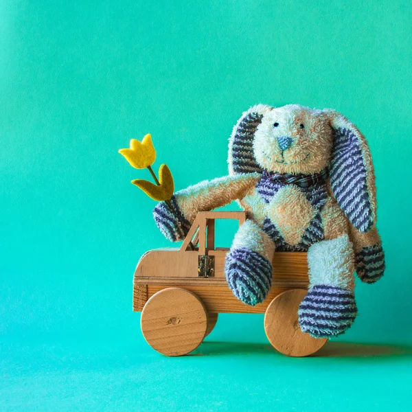 Cute teddy rabbit with yellow tulip on the wooden car. — Stock Photo, Image