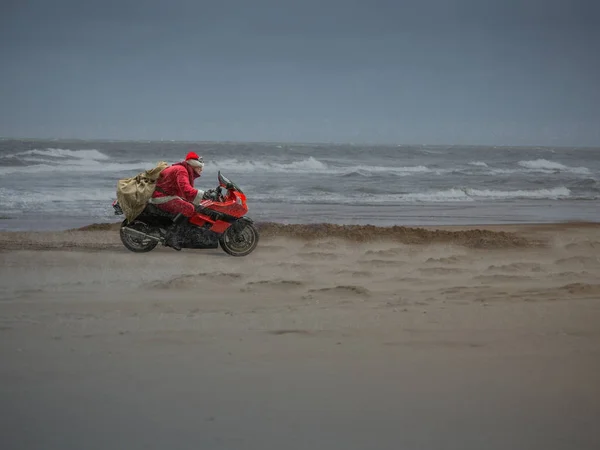 Santa Claus on a motorcycle drives fast along the winter beach.