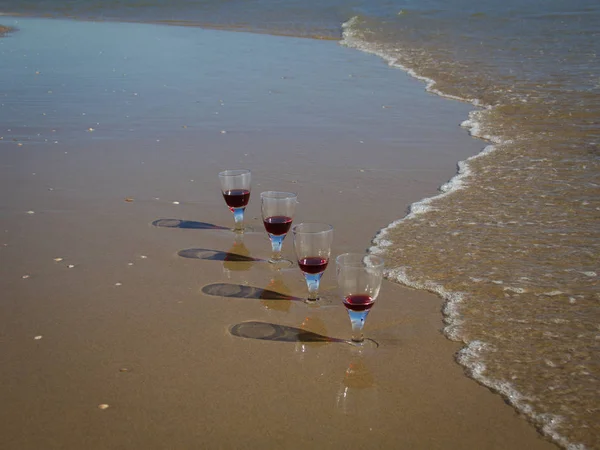 Four glasses of red wine in the wet sand of the sea coast — Stock Photo, Image