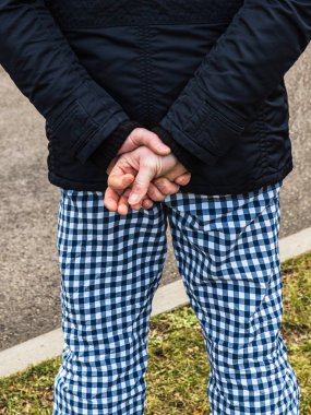 Damalı pantolonlu adam ellerini arkadan tutuyor..