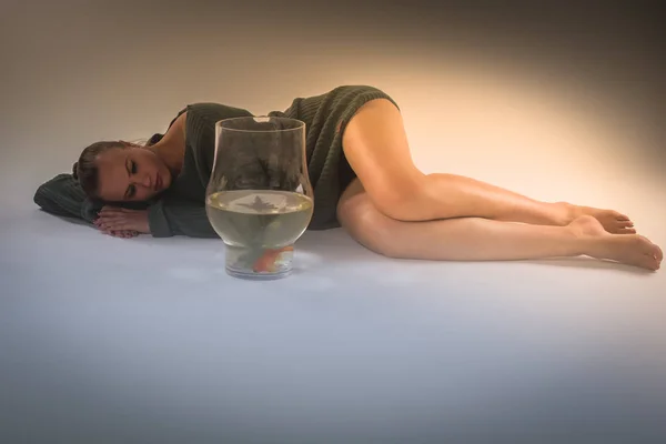 stock image young woman lying down on the floor and looking at goldfish in a