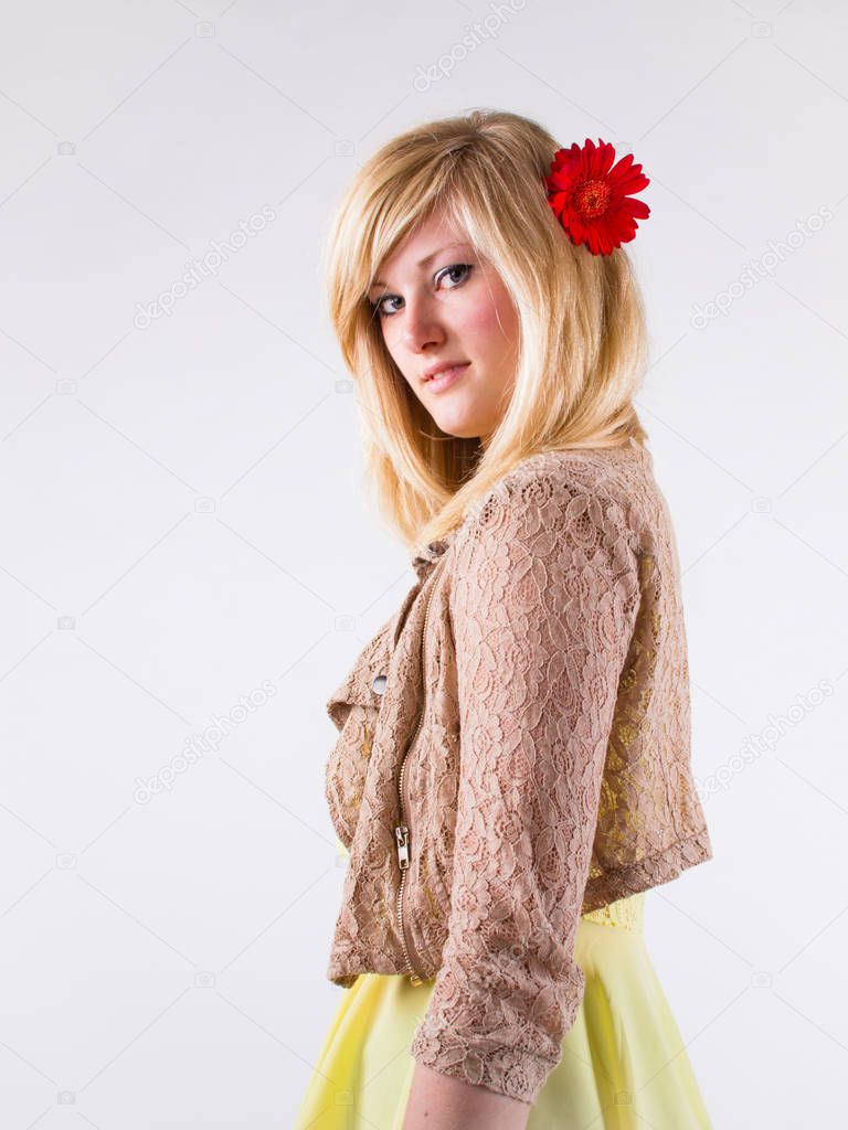 Young blonde with a red gerbera flower in her straight hair, sta