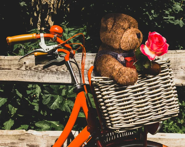Niedlichen Teddybär mit einer Rose in einem Korb ein orangefarbenes Fahrrad. Konzepte — Stockfoto