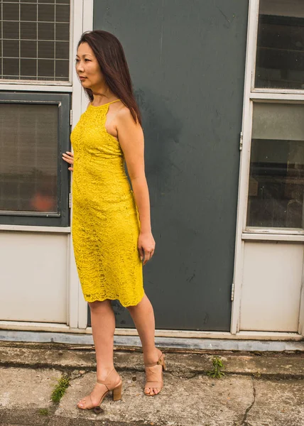 Intelligent elegant forty year old asian woman  with long hair against the background of an old gray door.  Outside shot.