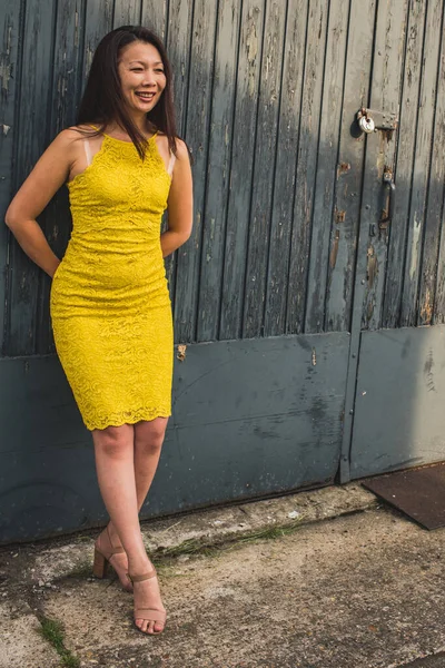 Elegant Asian model of 40 years in a yellow lace dress on the background of a rough textured wooden door. Outer shot in old area.