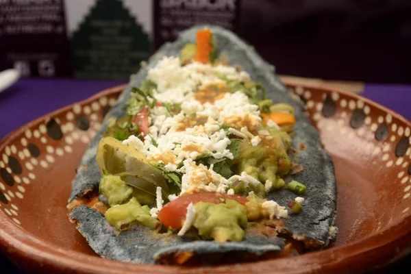Mexikói tlacoyos, egy tál készült kék kukorica és tele sült bab vagy a lóbab, hasonlít a mexikói gordita, guacamole, fűszeres mártással, koriander és sajttal a tetején — Stock Fotó