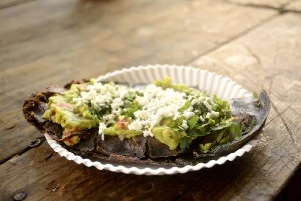 Tlacoyos mexicanos, um prato feito com milho azul e cheio de feijão frito ou feijão largo, semelhante ao gordita mexicano, com guacamole, molho picante, coentro e queijo no topo — Fotografia de Stock