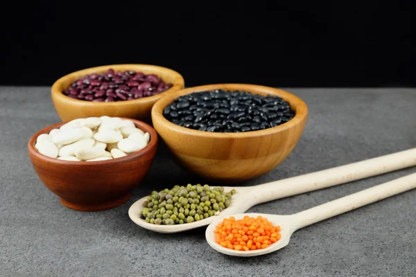 Vários tipos de feijões e lentilhas em uma tigelas de madeira e colheres . — Fotografia de Stock