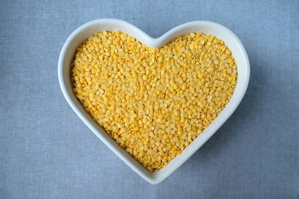Lentilhas amarelas em uma tigela em forma de coração . — Fotografia de Stock