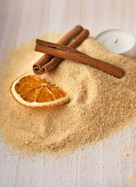 Esmer şeker, tarçın çubukları, şekerli portakal ve hafif ahşap arka planda bir mum.