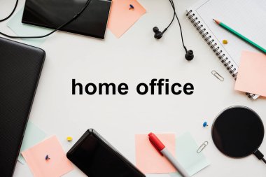 Laptop, akıllı telefon, elektrik bankası, kablosuz şarj, kulaklık ve kırtasiye malzemesi beyaz bir masada. Coronavirus salgını sırasında evden ofise.