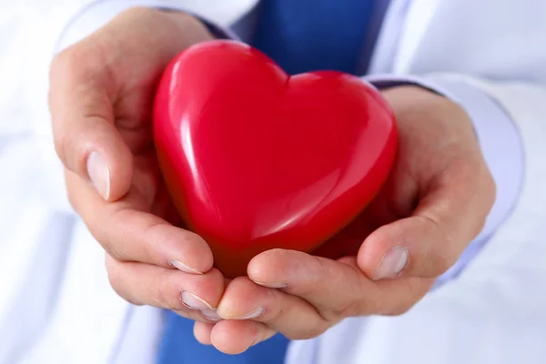 Médico masculino manos sosteniendo y cubriendo corazón de juguete rojo —  Fotos de Stock