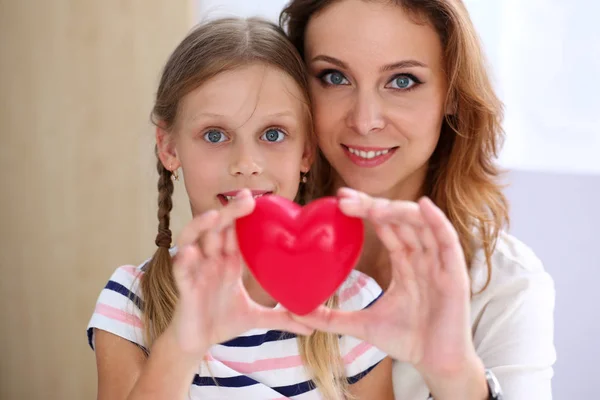 Hermosa mujer sonriente y niño sostienen corazón de juguete rojo —  Fotos de Stock