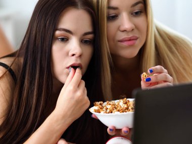 İki mutlu gülümseyen kız yatakta patlamış mısır yemek