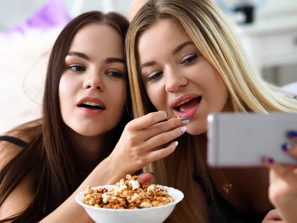 Two happy smiling girlfriends eat popcorn