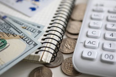 Yüz Amerikan doları banknotlar beyaz hesap makinesiyle not defterinde yatıyor.