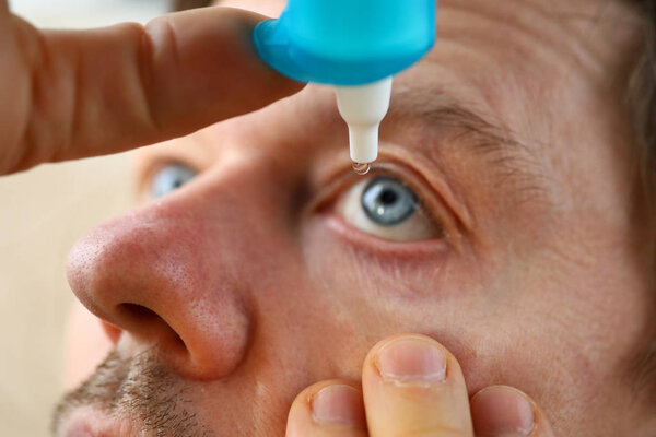 Male hand putting liquid drops in his eye