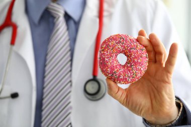 Ofisteki doktor elinde pembe donut tutuyor.