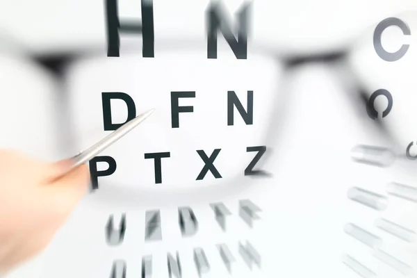 Srebrny długopis wskazujący na literę w tabeli kontrolnej przez okulary — Zdjęcie stockowe