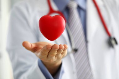 Erkek doktor el ele tutuşup kırmızı oyuncak kalbi kapatıyor.