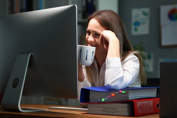 Žena pije čaj, usmívá se při pohledu na monitor — Stock fotografie