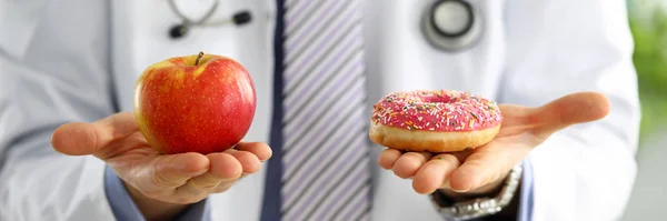 Γιατρός στο γραφείο κρατώντας στο χέρι ροζ ντόνατ vs κόκκινο μήλο — Φωτογραφία Αρχείου