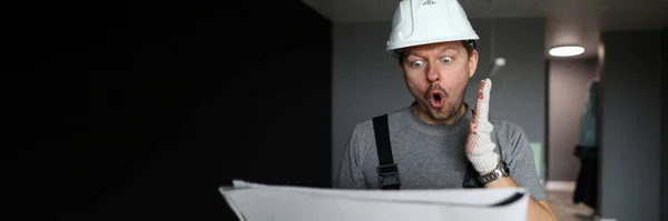 Jovem reparador de pé em apartamento vazio, olhando para o plano de construção e se sentindo chocado — Fotografia de Stock