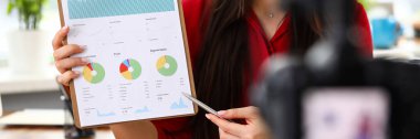 Kameranın karşısında oturan ve istatistik ve analitik raporlar sunan genç bir kadın.