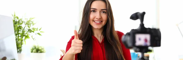 Giovane donna seduta in ufficio di fronte alla fotocamera e mostrando buona fortuna pollice dito in su — Foto Stock