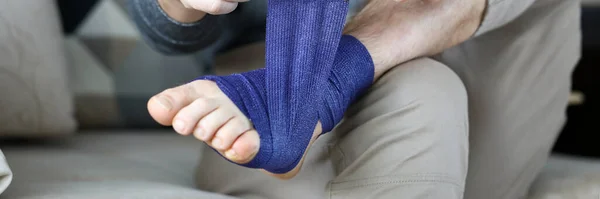 Man give himself first aid rolling blue bandage tape over foot