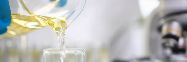 Científico mano usando guantes protectores vertiendo un poco de líquido amarillo en el laboratorio — Foto de Stock