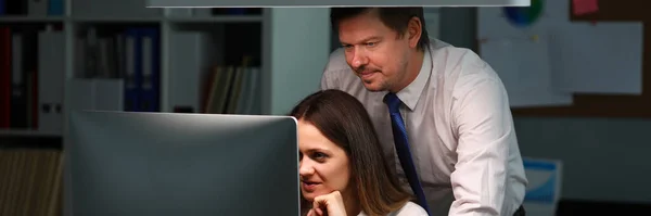 Woman shows man in office information on monitor
