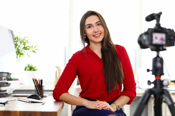 Mladá žena sedí v kanceláři naproti kameře na stativu — Stock fotografie