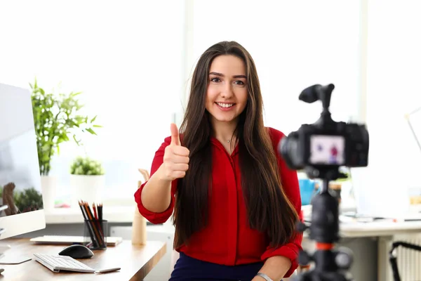Молода жінка сидить в офісі навпроти камери і показує удачу великий палець вгору — стокове фото