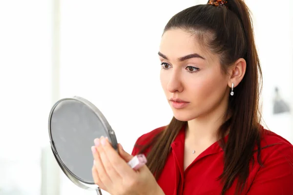 Giovane bella donna bruna in camicia rossa guardando lo specchio in ufficio — Foto Stock