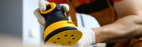 Male construction worker wearing hardhat and protective mask using sanding machine