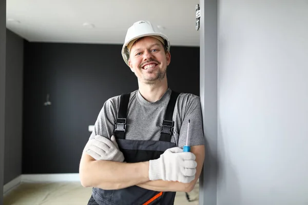 Jovem reparador sorridente em pé em apartamento vazio e segurando chave de fenda nas mãos — Fotografia de Stock