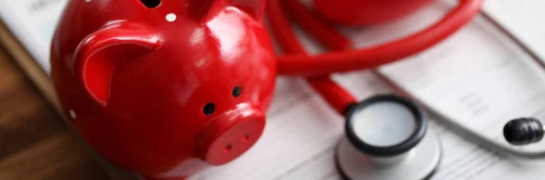 Red piggy bank stethoscope and toy heart lying at health insurance claim form — Stock Fotó