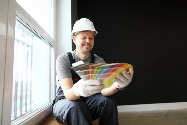 Молодой ремонтник в шлеме сидит в квартире и выбирает цвет для интерьера — стоковое фото
