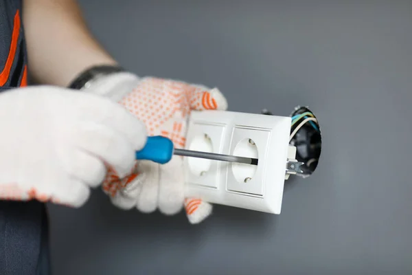 Ремонтник в перчатках, закрепляющий розетку с отверткой — стоковое фото