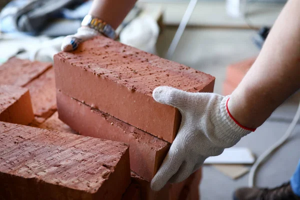 Mains masculines soulevant plusieurs briques rouges sur le chantier — Photo