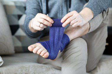 Adam kendine ilk yardım paketi yaptı. Mavi bandajı ayağıyla sardı.