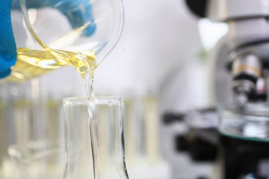 Koruyucu eldivenler giyen bilim adamı laboratuvara biraz sarı sıvı döküyor.