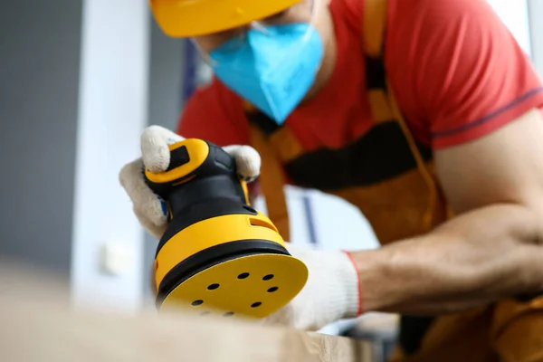 Pekerja konstruksi pria mengenakan topi keras dan masker pelindung menggunakan mesin sanding — Stok Foto