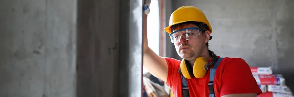 Builder in helmet measures level wall at window