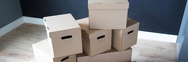 Pile of carton boxes standing in the middle of empty room in new house — Stock Photo, Image