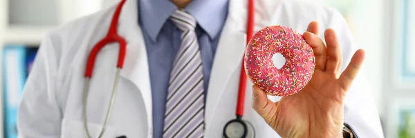 Lekarz w biurze trzyma w ręce różowego pączka — Zdjęcie stockowe