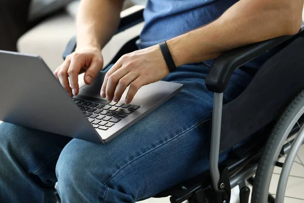 Человек, сидящий в инвалидной коляске и работающий с ноутбуком — стоковое фото