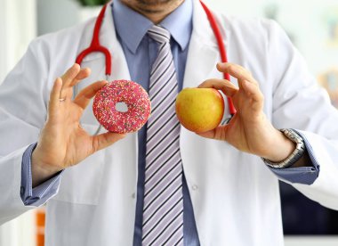 Ofisteki doktor elinde pembe çörekle kırmızı elmaya karşı
