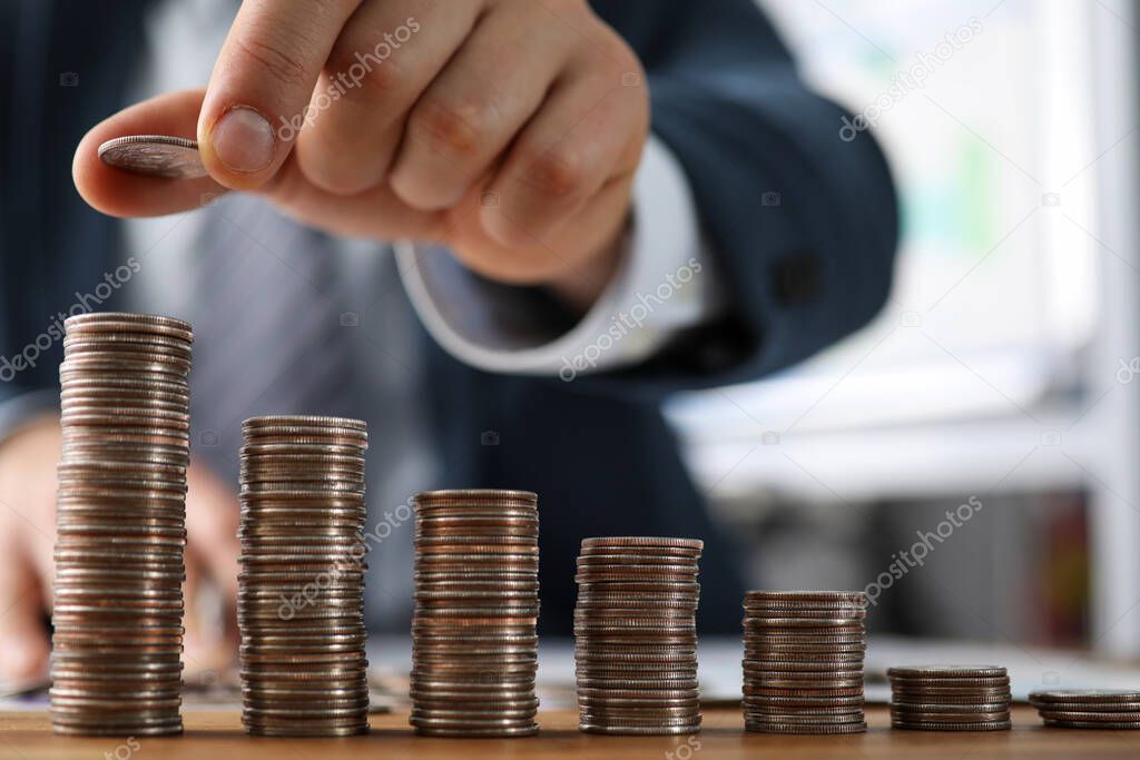 Male hands in suit stack coins on table, saving